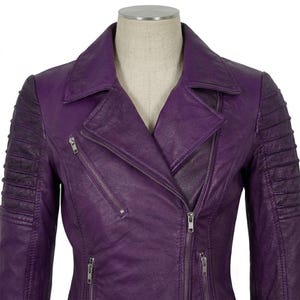Puede incluir: Una chaqueta de color morado vibrante con cuello de solapa clásico, cierre de cremallera frontal asimétrico y tres bolsillos con cremallera adicionales. Las mangas presentan detalles acolchados horizontales en la parte superior.