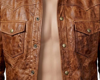 May include: A tan brown jacket with a distressed, textured finish. The garment features a pointed collar, a front button-down closure with metallic snaps, and two chest pockets with buttoned flaps. The design includes western-style yokes.