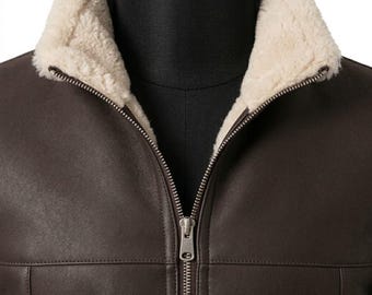 May include: A dark brown jacket featuring a cream-colored faux shearling collar and interior lining. The garment includes a central silver-toned metal zipper closure that extends from the collar down the front, with visible stitching.