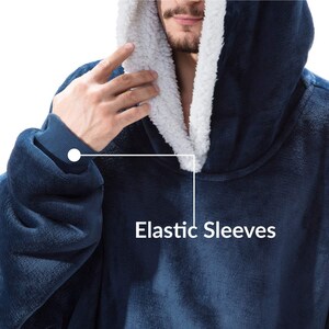 Peut inclure: Une couverture &agrave; capuche bleu marine avec une doublure int&eacute;rieure blanche et moelleuse. La couverture a des manches &eacute;lastiques et est faite d'une mati&egrave;re douce et moelleuse. Le texte "Elastic Sleeves" est visible sur l'image.
