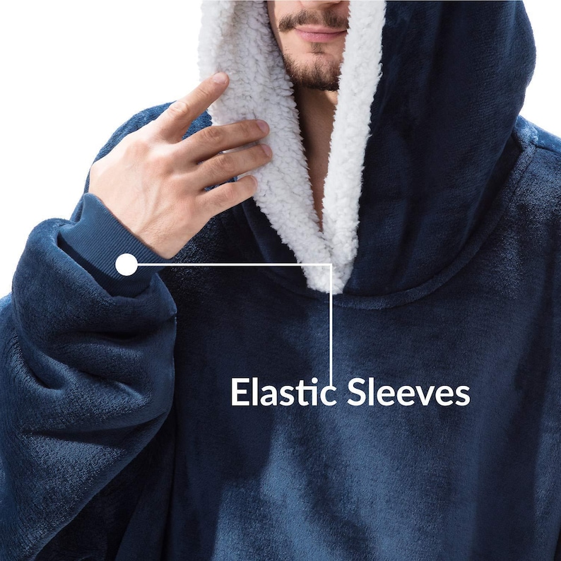 Peut inclure: Une couverture &agrave; capuche bleu marine avec une doublure int&eacute;rieure blanche et moelleuse. La couverture a des manches &eacute;lastiques et est faite d'une mati&egrave;re douce et moelleuse. Le texte "Elastic Sleeves" est visible sur l'image.