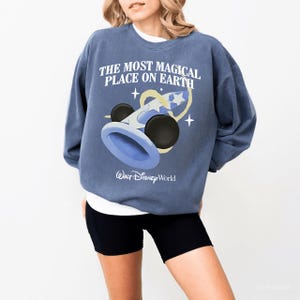 May include: A blue sweatshirt with the text "THE MOST MAGICAL PLACE ON EARTH" and a graphic of a wizard hat and stars. The words "Walt Disney World" are printed below the graphic.