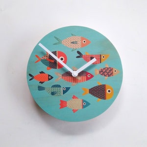 May include: A turquoise round clock with white hands and a design of colorful fish on a turquoise background.