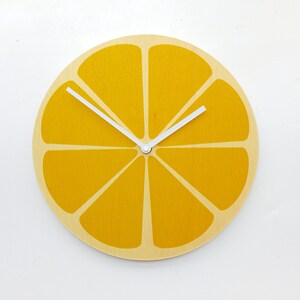 May include: A yellow wooden clock shaped like a slice of lemon with white hands.