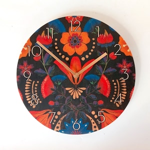 May include: A round clock with a black background and colorful floral design. The clock face has Roman numerals and gold hands.