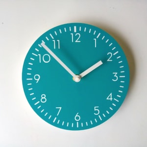 May include: A teal blue round clock with white numbers and hands. The clock face has a white outline and white markings for the minutes.