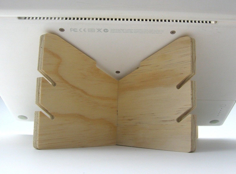May include: A wooden laptop stand with a triangular shape and cutouts. The stand is made of light-colored wood and is designed to elevate a laptop for better ergonomics.