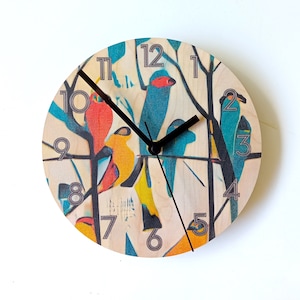 May include: A round wooden clock with a colourful design featuring birds and branches. The clock face has black hands and Roman numeral hour markers.