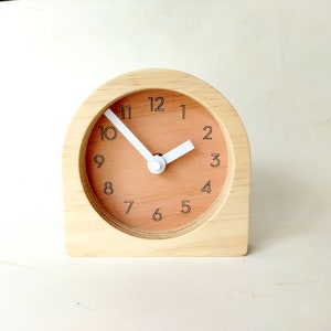May include: A wooden clock with a light brown face and white hands. The clock has black numbers and is set to 10:10.