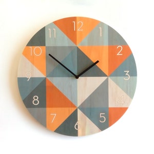 May include: A round clock with a geometric design featuring orange and blue triangles. The clock face has white numbers 1 through 12 and black hands.