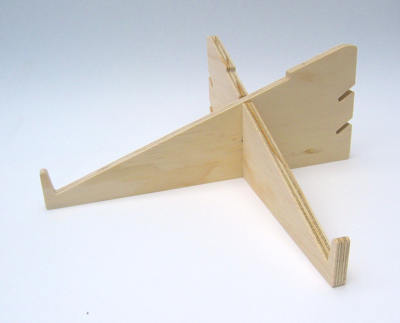 May include: A wooden laptop stand with a simple, minimalist design. The stand is made of light-colored wood and has a cross-shaped base.
