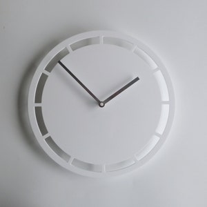 May include: A white round clock with silver hands and a unique design featuring rectangular cutouts around the face.
