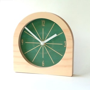 Puede incluir: Un reloj de madera con una esfera verde y agujas blancas. El reloj tiene un diseño sencillo con números dorados y un acabado de madera.