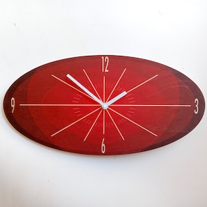 May include: A red oval clock with white hands and black Roman numeral markings. The clock face has a radial design with a red background.
