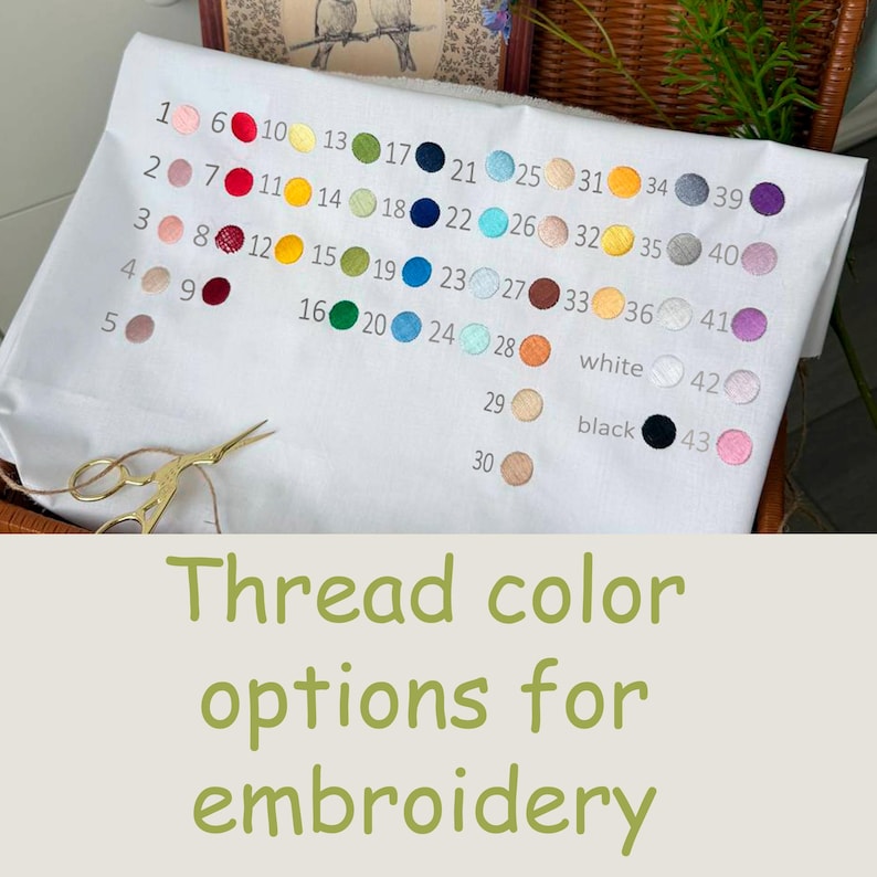 May include: White fabric with a color chart of embroidery thread options. The chart displays 43 thread colors, numbered and arranged in rows. Gold scissors are on the left. Text reads: "Thread color options for embroidery."