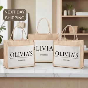 Three beige tote bags with the word "OLIVIA" printed on them, placed on a white countertop.