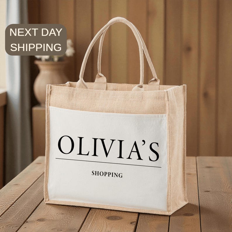 A beige tote bag with the text "OLIVIA'S SHOPPING" printed on it, sitting on a wooden surface.
