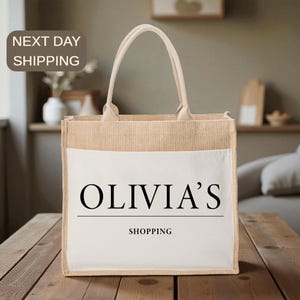 A beige tote bag with the text "OLIVIA'S SHOPPING" printed on it, placed on a wooden surface.