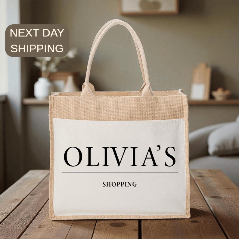 A beige tote bag with the text "OLIVIA'S SHOPPING" printed on it, placed on a wooden surface.