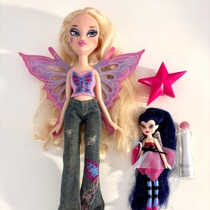 May include: Two Bratz dolls, one large and one small, with accessories. The larger doll has blonde hair, pink butterfly wings, and denim pants. The smaller doll has dark blue hair and a pink dress. A pink star and a small bottle are also present.