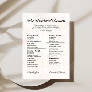 May include: A white wedding itinerary card with the text "The Weekend Details" and event times. The card lists the wedding ceremony, reception, and other events. The names "Emma & James" are at the bottom.