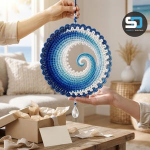 Peut inclure: Une décoration murale circulaire en crochet présentant un motif en spirale dans des tons de bleu et de blanc, avec un bord festonné. L'objet est suspendu par un cordon bleu avec une perle en cristal en haut et un pendentif en cristal en forme de goutte.