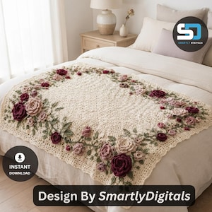 May include: A cream-colored crochet blanket featuring a decorative border of three-dimensional roses in shades of deep burgundy, dusty pink, and soft blush, accented with green crocheted leaves and vines, laid flat across a neutral-toned bedspread.