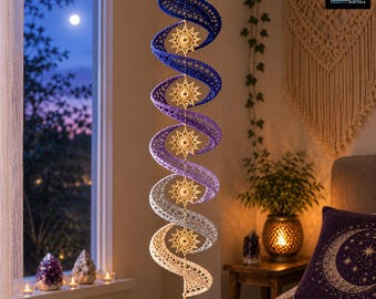 Könnte beinhalten: Ein hängendes Spiral-Mobile mit einem Häkel-Farbverlauf von Dunkelblau bis Hellcreme. Fünf komplizierte, sternförmige Häkelmedaillons sind entlang der Mitte befestigt, und ein klarer, facettierter Kristall-Tropfen hängt am unteren Ende.