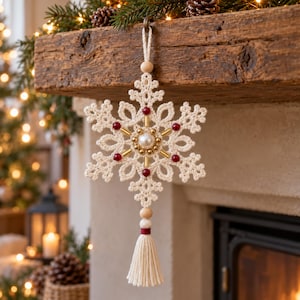 May include: A cream-colored crocheted snowflake ornament featuring a central white pearl bead surrounded by small gold beads. The snowflake is accented with six dark red beads and hangs from a loop with a matching cream-colored yarn tassel.