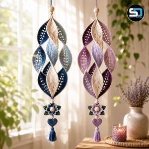 May include: Two hanging crochet ornaments featuring a twisted leaf-like structure. One ornament displays shades of blue and cream, while the other features purple and cream. Each piece is accented with a crocheted flower, a heart, and a tassel.