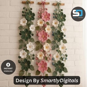 May include: Three vertical wall hangings featuring crocheted flowers and leaves in shades of dark green, light pink, and white. Each piece is suspended from a small wooden dowel with yarn. The text "Design By SmartlyDigitals" is visible.