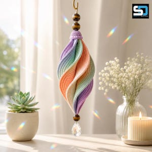 May include: A hanging ornament featuring a spiraling, multi-colored crochet fabric structure in pastel shades of lavender, mint green, and peach. It is accented with two brown tiger eye beads at the top, one at the bottom, and a clear crystal teardrop.