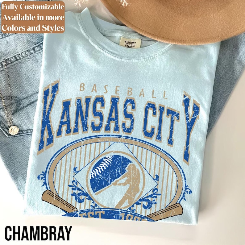 May include: Light blue t-shirt with a distressed graphic that says "Baseball Kansas City" in blue and tan. The shirt features a baseball and a batter illustration. The word "Chambray" is at the bottom.