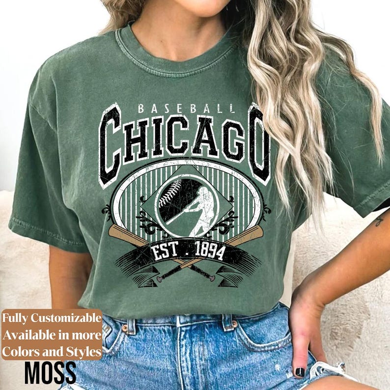 May include: Green t-shirt with a baseball-themed graphic. The design features the word "Chicago" in a bold font, a baseball, a batter silhouette, and the text "EST 1894". The shirt is a moss green color.