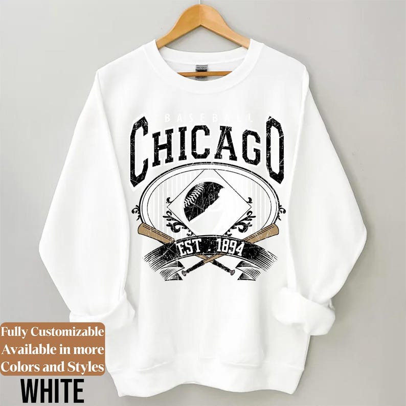 May include: White sweatshirt with a baseball-themed graphic. The design features the word "CHICAGO" in a distressed font, a baseball, crossed bats, and the text "EST. 1894". The sweatshirt is hanging on a wooden hanger.