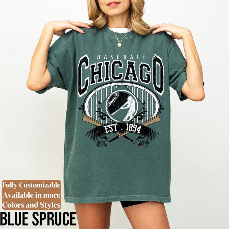 May include: Blue spruce-colored t-shirt with a baseball-themed graphic. The design features the word "CHICAGO" in a vintage font, along with a baseball, a batter silhouette, and crossed bats. The text "EST. 1894" is also included.