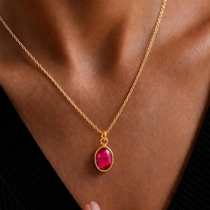 Può includere: Una collana a catena dorata con un singolo ciondolo di forma ovale caratterizzato da una gemma sfaccettata color rosa intenso incastonata in una montatura dorata. Il ciondolo pende da una sottile catena a maglie dorate con finitura lucida.