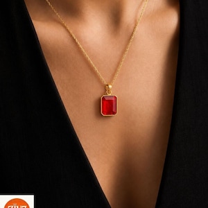 Op de afbeelding: Een gouden ketting met een rechthoekige, gefacetteerde rode edelsteen hanger in een gouden zetting. De hanger hangt aan een fijne gouden schakelketting. Het logo ZIV7 is zichtbaar in de linkerbenedenhoek van de afbeelding.