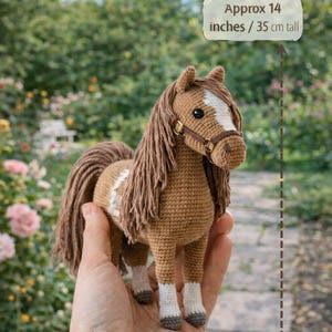 Peut inclure: Cheval en crochet marron avec des marques blanches, une longue crinière et une queue. Il mesure environ 35 cm de haut. Le texte indique : « Environ 14 pouces / 35 cm de haut ».