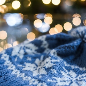 Pu&ograve; includere: Un cappello blu lavorato a maglia con un motivo a fiocco di neve bianco. Il cappello &egrave; morbido e confortevole, perfetto per l'inverno.