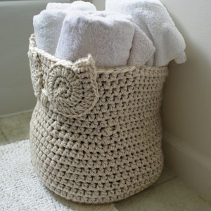 May include: A crocheted owl-shaped basket filled with white towels in a bathroom setting.