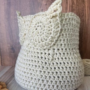 May include: A crocheted owl-shaped basket made of beige yarn. The basket has a round body and two large ears.