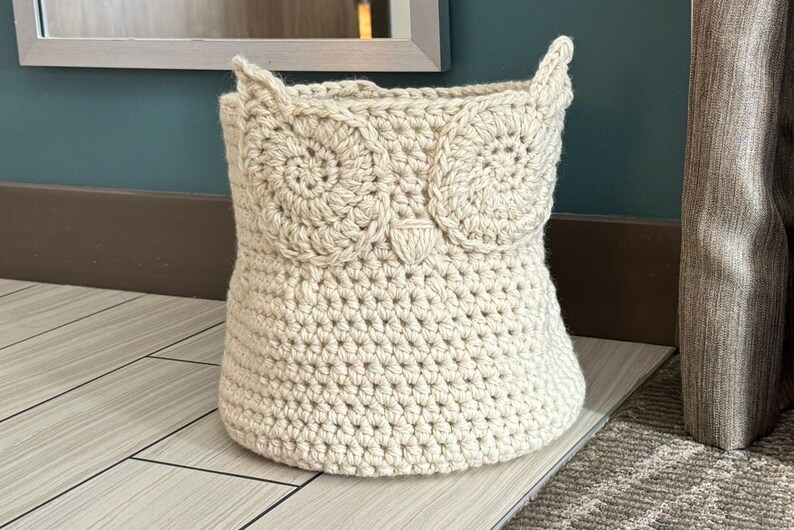 May include: A crocheted owl-shaped basket in a cream color. The basket is made of yarn and has a textured surface.