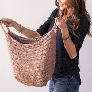 May include: A woman holds a large, knitted, beige tote bag. The bag is made with a simple stitch pattern and has a wide, open top.