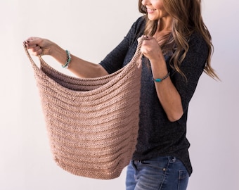 May include: A woman holds a large, knitted, beige tote bag. The bag is made with a simple stitch pattern and has a wide, open top.
