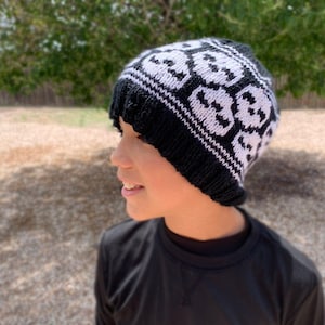 May include: A black and white knit beanie with a skull pattern. The beanie is worn by a child.
