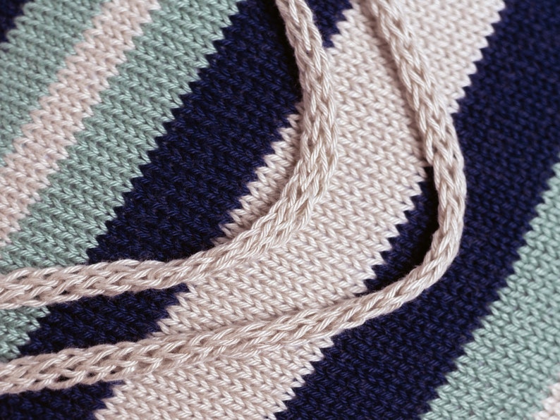 May include: Close-up of a knitted fabric with stripes of beige, blue, and green. The fabric is woven in a diagonal pattern, creating a textured look.
