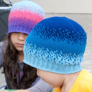 May include: Two children wearing colorful crocheted hats. The hat on the left is pink, purple, and blue. The hat on the right is blue, light blue, and white.