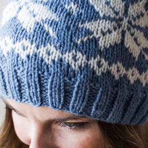 Pu&ograve; includere: Un cappello di lana blu e bianco con un motivo geometrico. Il cappello &egrave; indossato da una persona con i capelli castani.