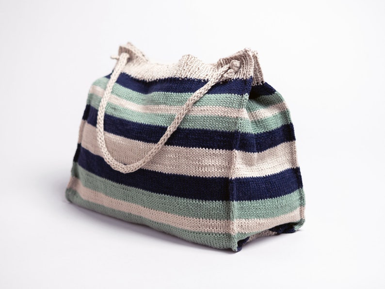 May include: A striped knitted tote bag with beige, blue, and green stripes. The bag has two long beige handles.
